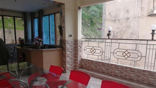 A dining area with red chairs and a glass table, a brick wall, and a balcony with a metal railing. - Valley View Hotel & Restaurant (Balakot)