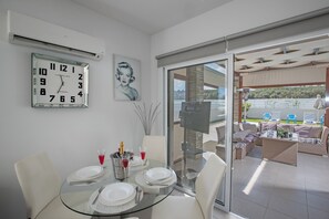 Un coin repas avec une table en verre, des chaises blanches et une horloge fixée au mur.