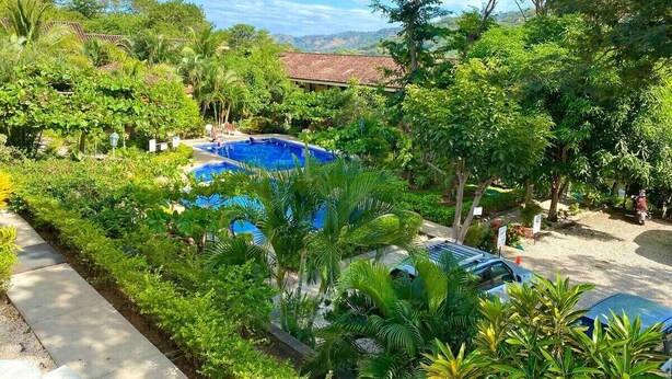 Ein Pool, umgeben von üppiger Vegetation, einem klaren blauen Himmel und einer entfernten Bergkette.