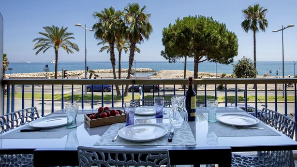 An outdoor dining area with a table set for two, overlooking a beach with palm trees and the sea. - Le Grand Large by Interhome (Cagnes-sur-Mer)