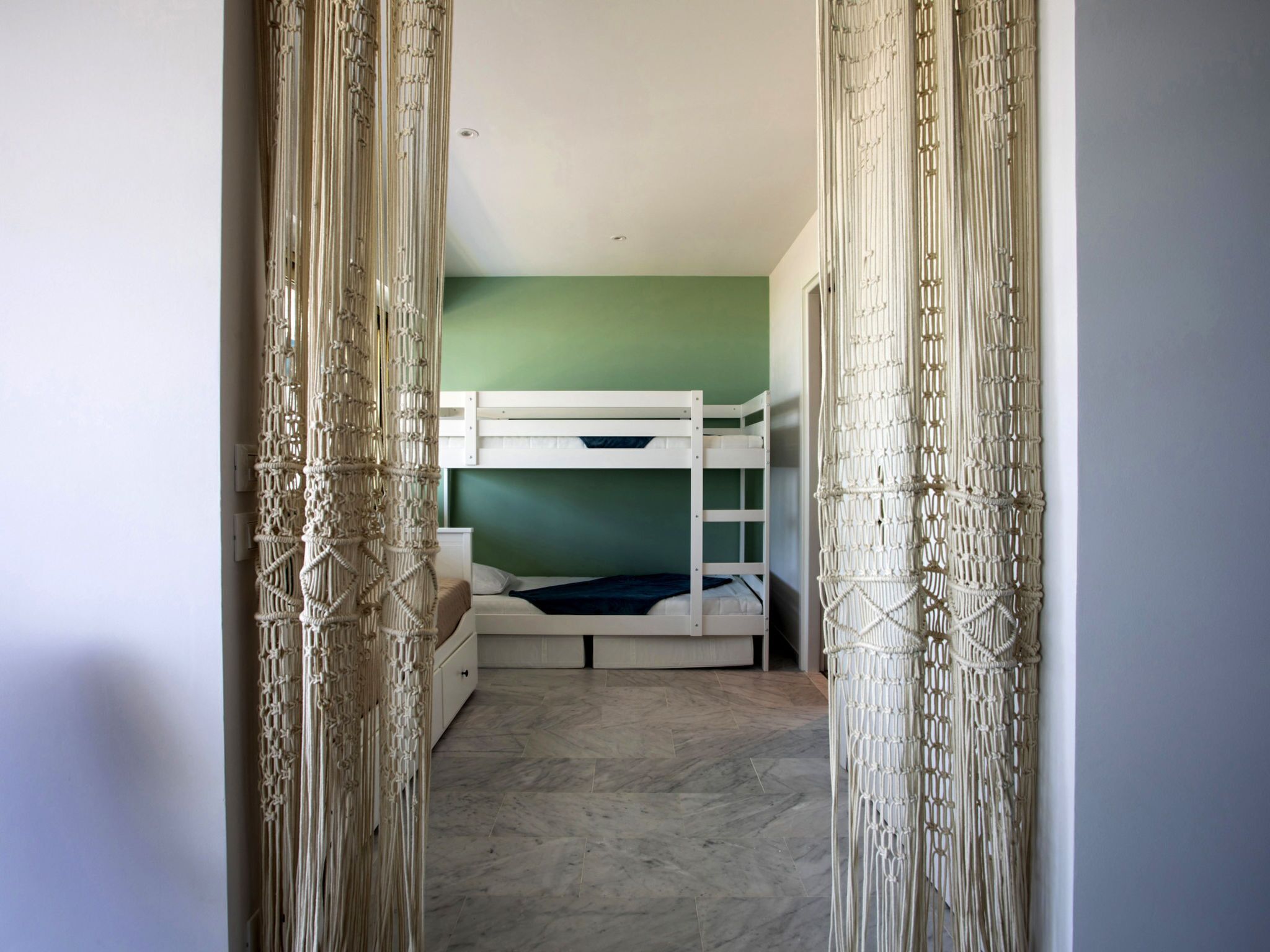 A room with bunk beds, a green wall, and macramé curtains.