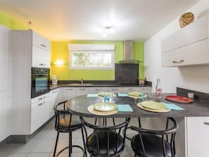 Uma cozinha moderna com uma ilha central, banquetas pretas e uma janela com vista para o verde.