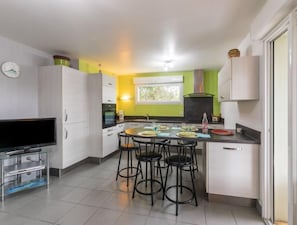 Uma cozinha compacta com área de refeições, armários brancos, televisão de tela plana e janela que traz luz natural.
