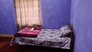 A small room with a single bed, a window with curtains, and a purple wall. - Seven Heaven Guest House (Kel)