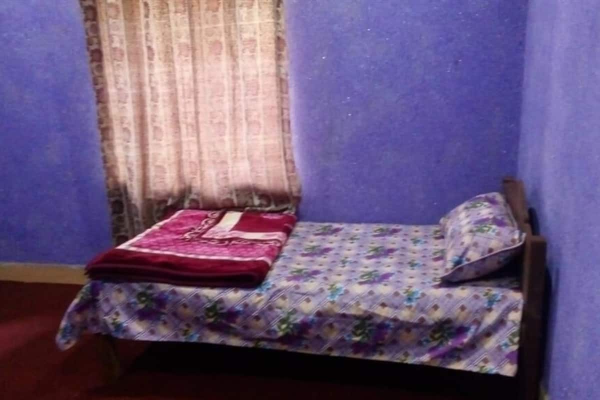 Quarto pequeno com uma cama de solteiro, uma janela com cortinas e uma parede roxa.