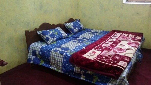 A bed with a blue and red patterned bedspread, two pillows, and a wooden headboard. - Seven Heaven Guest House (Kel)