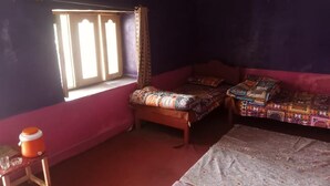 A bedroom with two beds, a window with curtains, a small table with a container, and a patterned rug. - Seven Heaven Guest House (Kel)