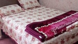 A bed with a floral bedspread and a red blanket, a wooden headboard, and patterned curtains. - Seven Heaven Guest House (Kel)