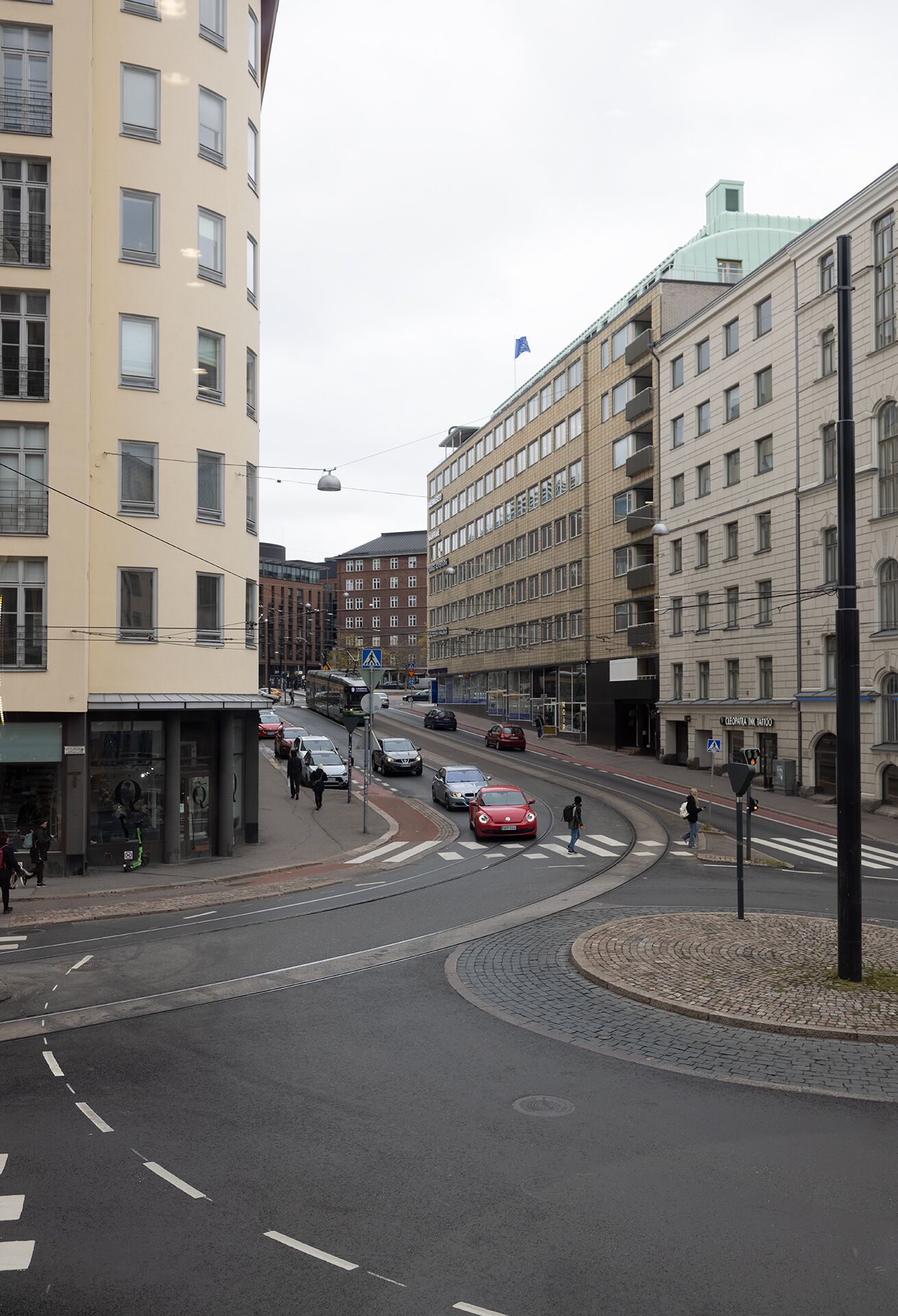 Ein mehrgeschossiges Gebäude mit Wohn- und Geschäftsflächen, einer Straßenbahnlinie und einem Fußgängerübergang.