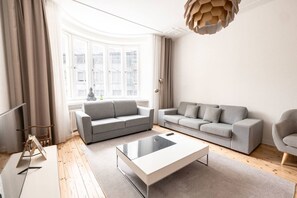A modern living room with two grey sofas, a glass coffee table, and a large window with curtains. - 2ndhomes Brand New 3BR Deluxe Apartment (Helsinki)