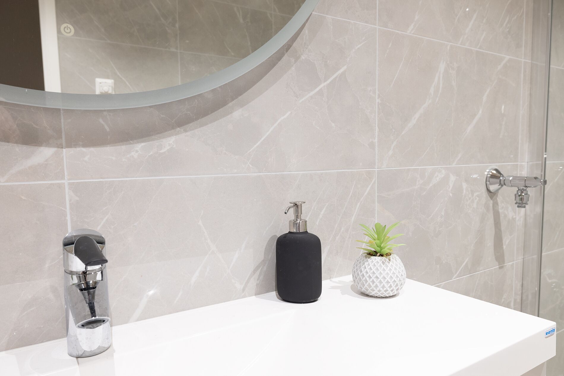 Un bagno con un lavandino bianco, un erogatore di sapone nero e una piccola pianta in vaso.