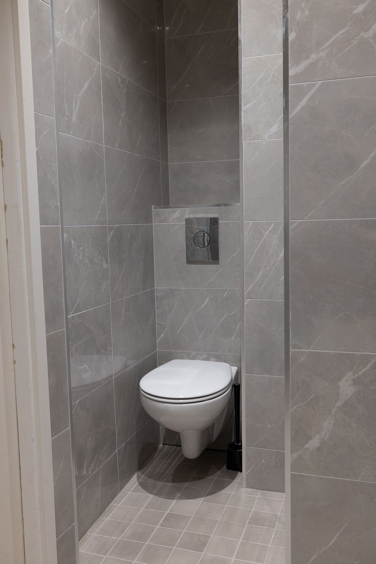 A small, modern bathroom with a toilet, a wall-mounted bidet, and a tiled floor.