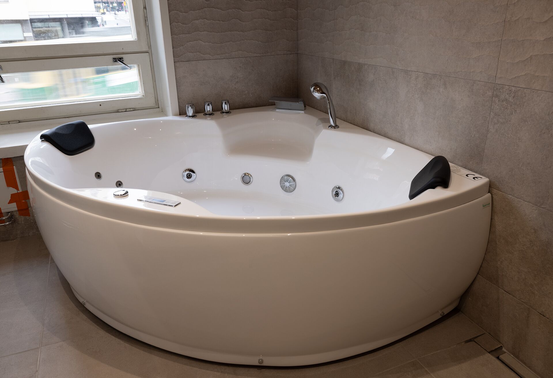 A large, white freestanding bathtub in a bathroom with a window and tiled walls.