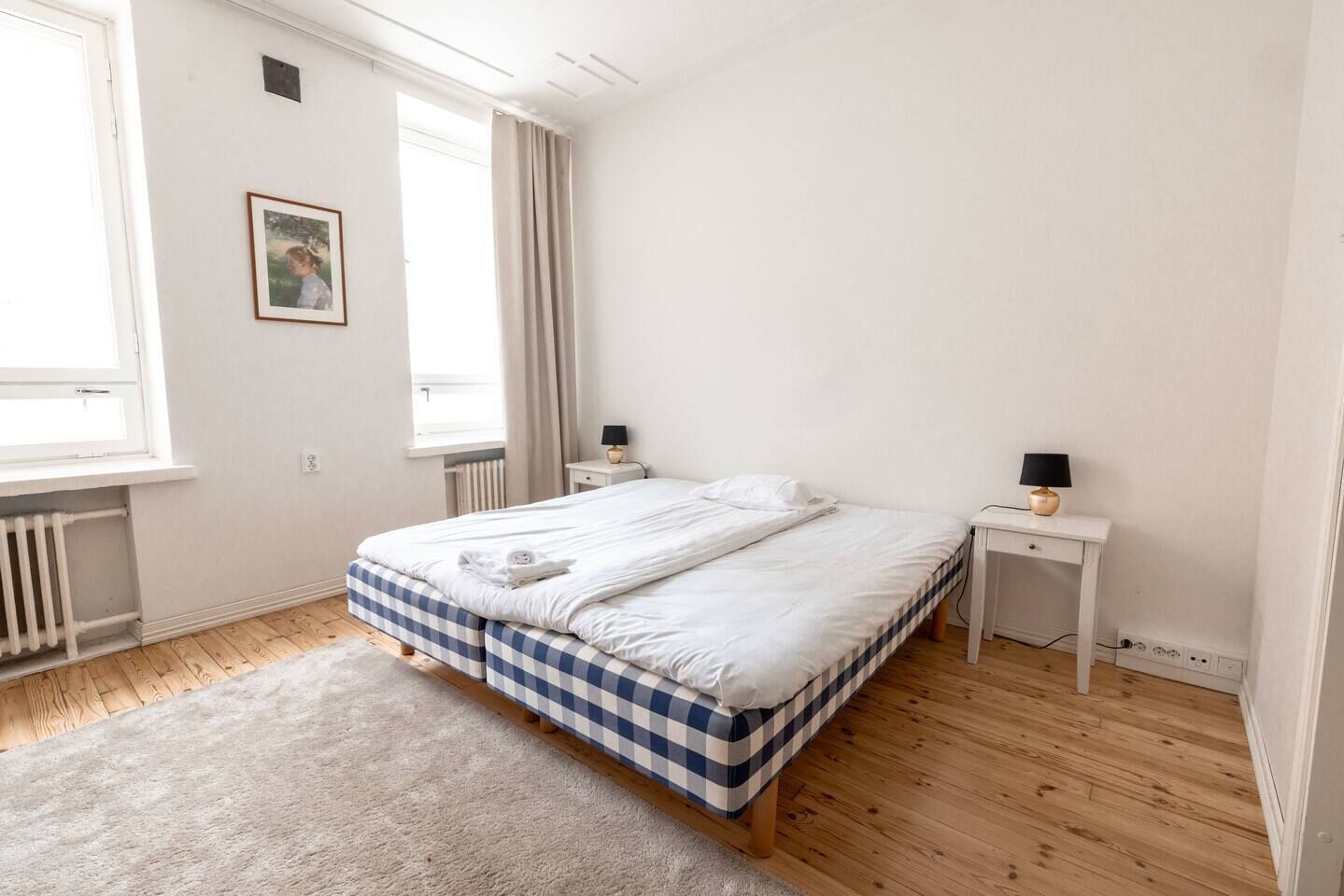 A bedroom with a bed, a bedside table, a lamp, a radiator, and a window.
