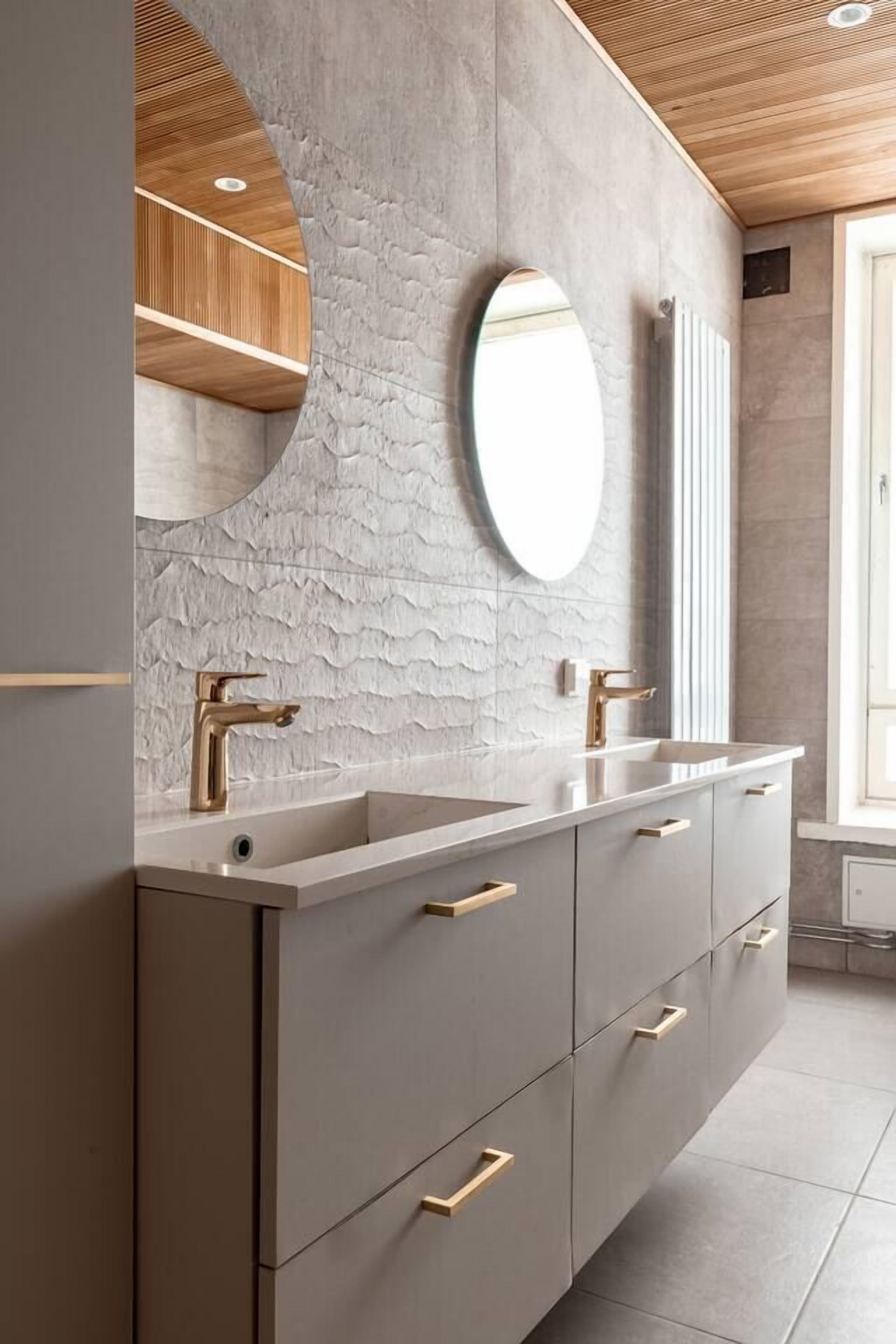 Une salle de bain moderne avec un grand miroir, deux lavabos et un mur à motifs.