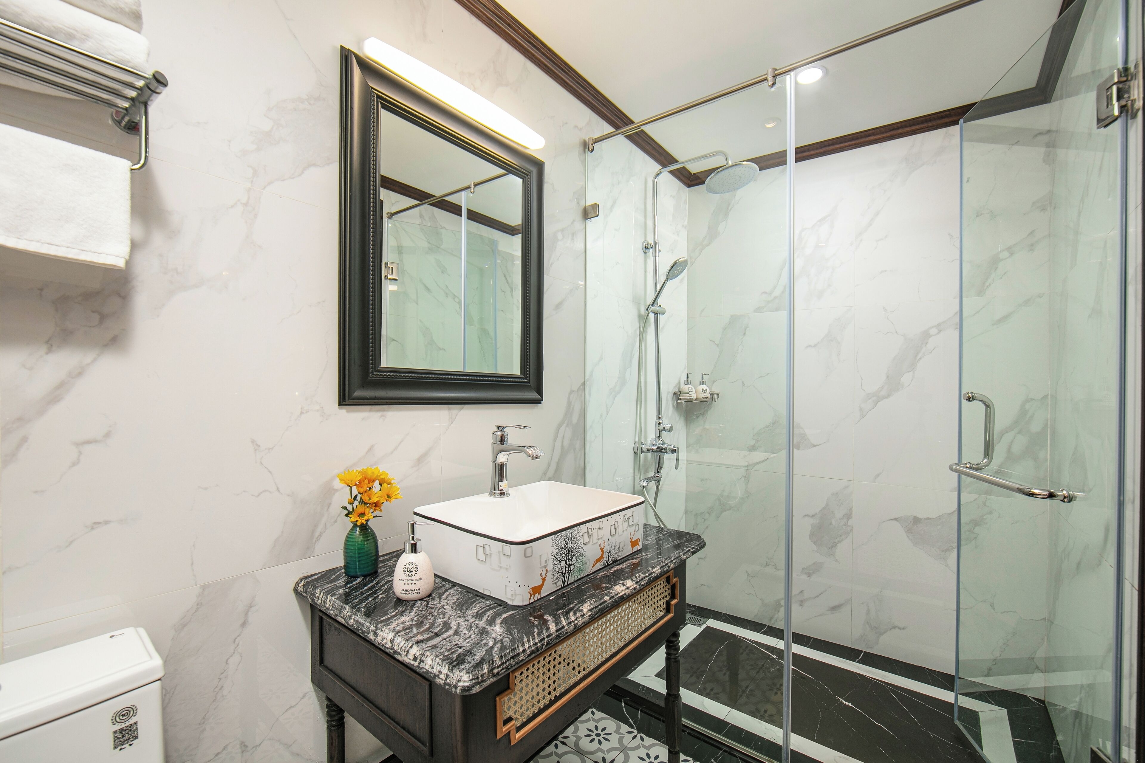 A bathroom with a marble wall, a glass shower enclosure, a white sink, and a mirror.