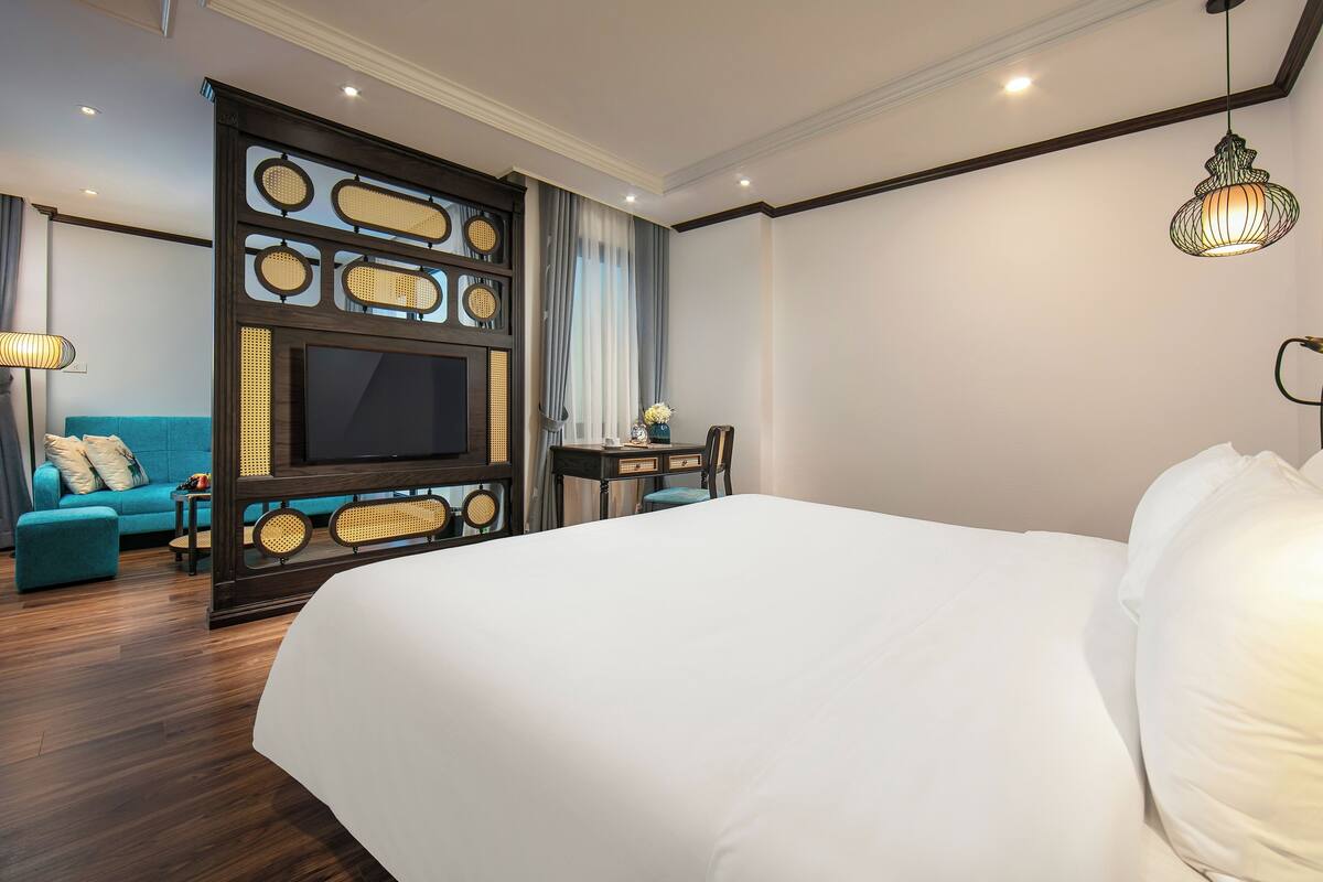 A hotel room with a large bed, a television, a seating area with a sofa and chairs, and a decorative wall panel.