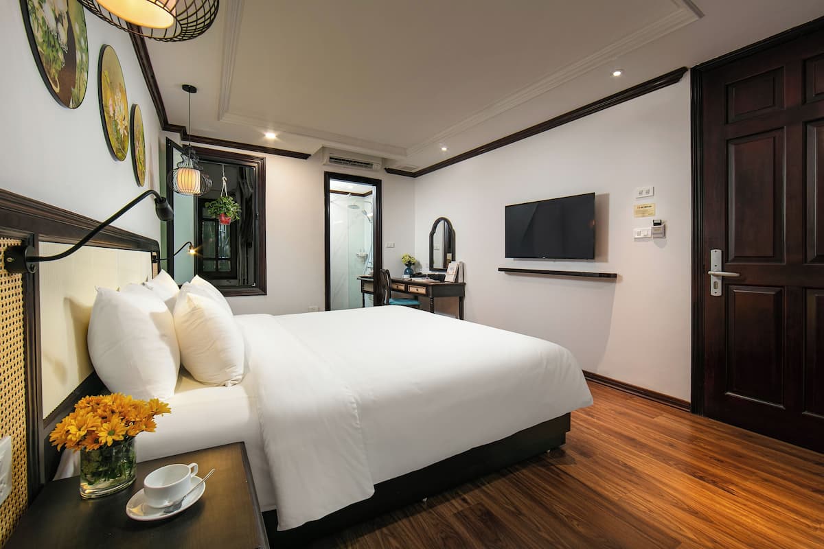 A hotel room with a large bed, a desk with a chair, a TV mounted on the wall, and a door.