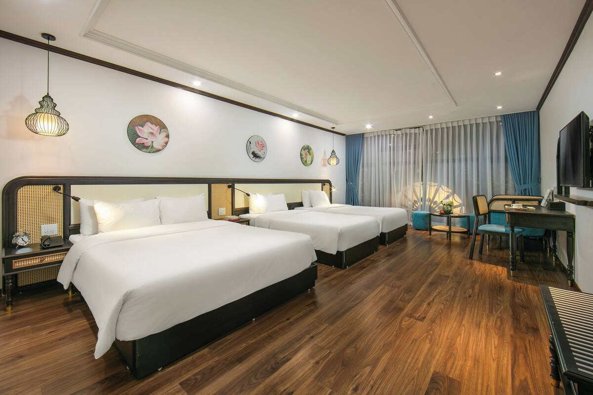 A hotel room with three beds, a desk, a chair, a television, and decorative wall art.