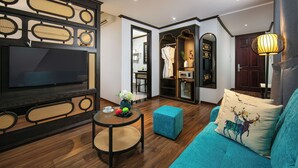 Una sala moderna con un televisor de pantalla plana grande, una mesa redonda con un florero y fruta, un sofá azul turquesa con un cojín decorativo, y piso de madera.