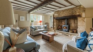 A cozy living room with exposed wooden beams, a stone fireplace, and comfortable seating. - Four bed Cotswold holiday cottage - Greenview Cottage (Little Barrington, near Burford)