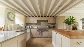 A kitchen with a central island, a stove, and a clock on the wall. - Four bed Cotswold holiday cottage - Greenview Cottage (Little Barrington, near Burford)
