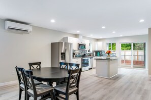 Une cuisine moderne avec des meubles blancs, des appareils en acier inoxydable et un coin repas comprenant une table ronde et des chaises.