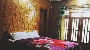 Un dormitorio con un diseño hexagonal de madera en la pared, una cama con una manta colorida y una ventana con persianas verticales.