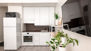 A modern kitchen with white cabinets, a built-in oven, a microwave, and a TV mounted on the wall. - 2ndhomes Modern Studio in the Center (Helsinki)