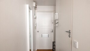 A hallway with a white door, a doormat with the word "welcome," and a small shelf with a telephone and a basket. - 2ndhomes Modern Studio in the Center (Helsinki)