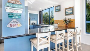 Uma cozinha moderna com uma parede de destaque azul, um espaço bar com cadeiras brancas e vista para o exterior.