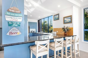 Une cuisine moderne avec un mur d’accent bleu, un coin bar avec des chaises blanches et une vue sur l’extérieur.
