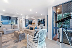 A modern living room with a telescope, two sofas, a dining area, and large windows.