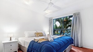 Quarto com cama, mesa de cabeceira, ventilador de teto e janela com cortinas.