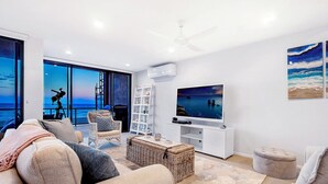 Uma sala de estar com uma grande janela com vista para o mar, televisão e um espaço de estar confortável.
