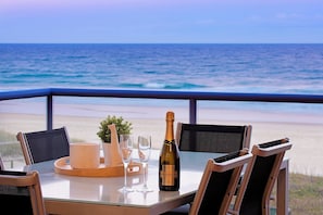 A table with a bottle of Chandon Brut wine, two glasses, a woven basket, and a small plant, set against a beach view.