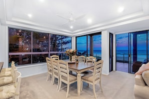 A dining area with a table and chairs, large windows with a view of the ocean, and a ceiling fan.