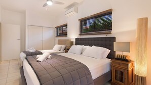 Een slaapkamer met een bed, nachtkastjes, een plafondventilator en een raam met jaloezieën.