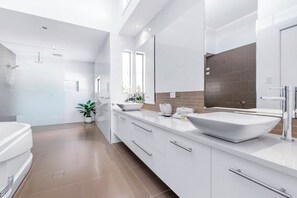 Un baño moderno con un espejo grande, dos lavamanos y una bañera.