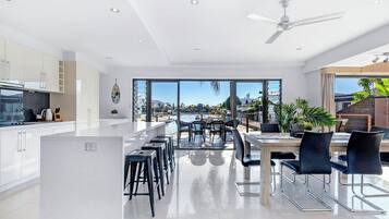 A modern kitchen with white cabinets, a dining area with a table and chairs, and large windows offering a view of the sea and buildings.