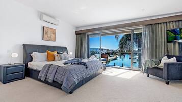 A modern bedroom with a large bed, a TV, and a view of a pool and buildings.