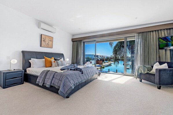 Un dormitorio moderno con una cama grande, un televisor y vistas a una piscina y edificios.
