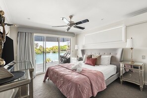 Un dormitorio con cama, ventilador de techo, mesita de noche, lámpara y vista a una masa de agua.