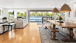 A spacious living area with a pool view, wooden flooring, and a dining area with a long table and benches. - Surfers Paradise Escape (Huge Heated Pool) (Gold Coast)