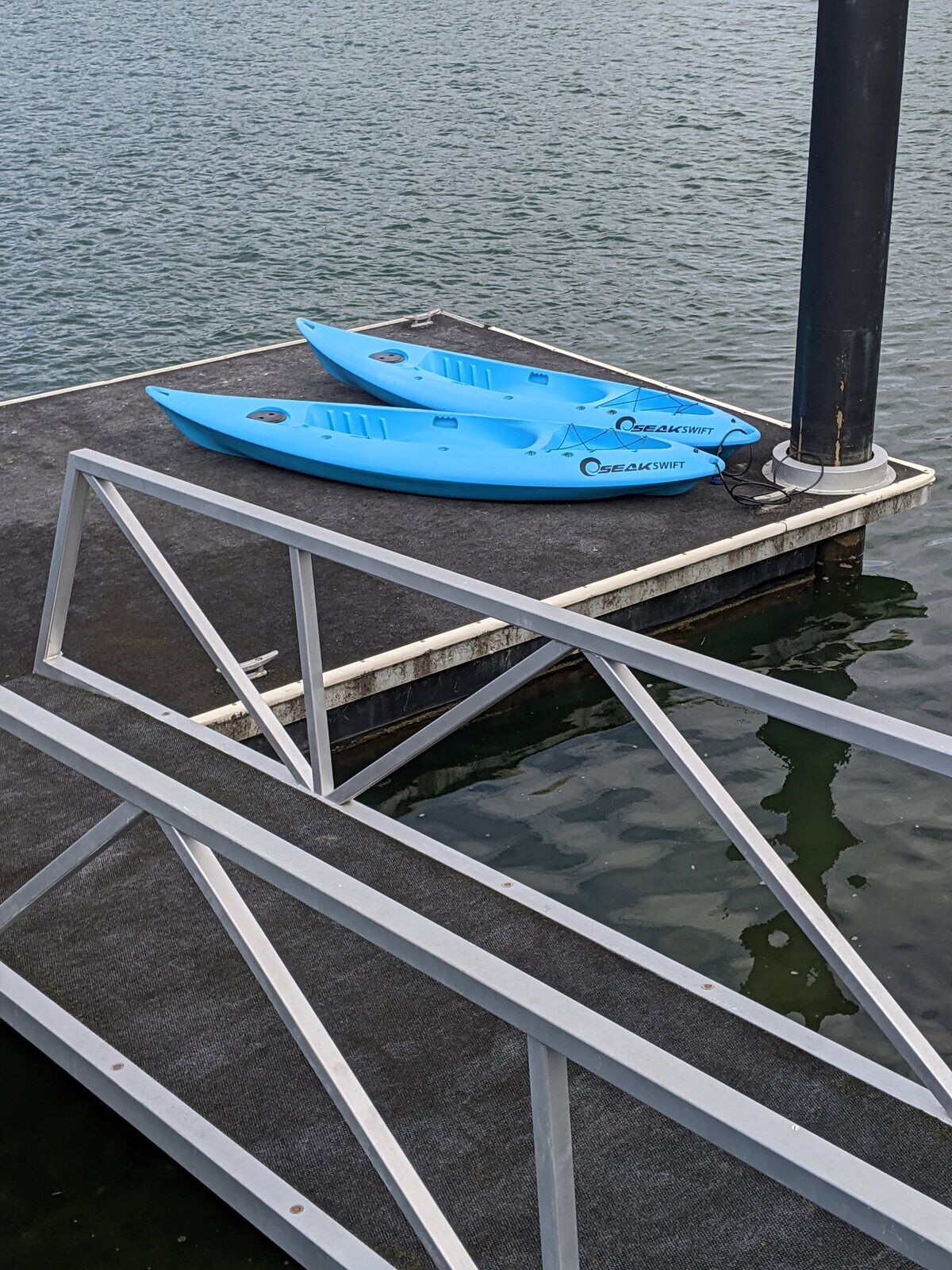 A dock with two blue kayaks and a metal railing.