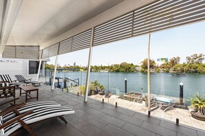 Un espacio lounge moderno al aire libre con asientos escalonados, vista a un río y un paisaje urbano de fondo.