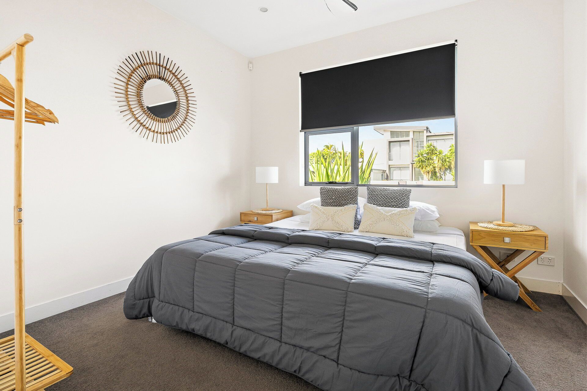 A bedroom with a bed, a window with a view, a bedside table, a lamp, and a wall-mounted mirror.