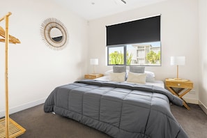 Ein Schlafzimmer mit Bett, Fenster mit Aussicht, Nachttisch, Lampe und einem Wandspiegel.