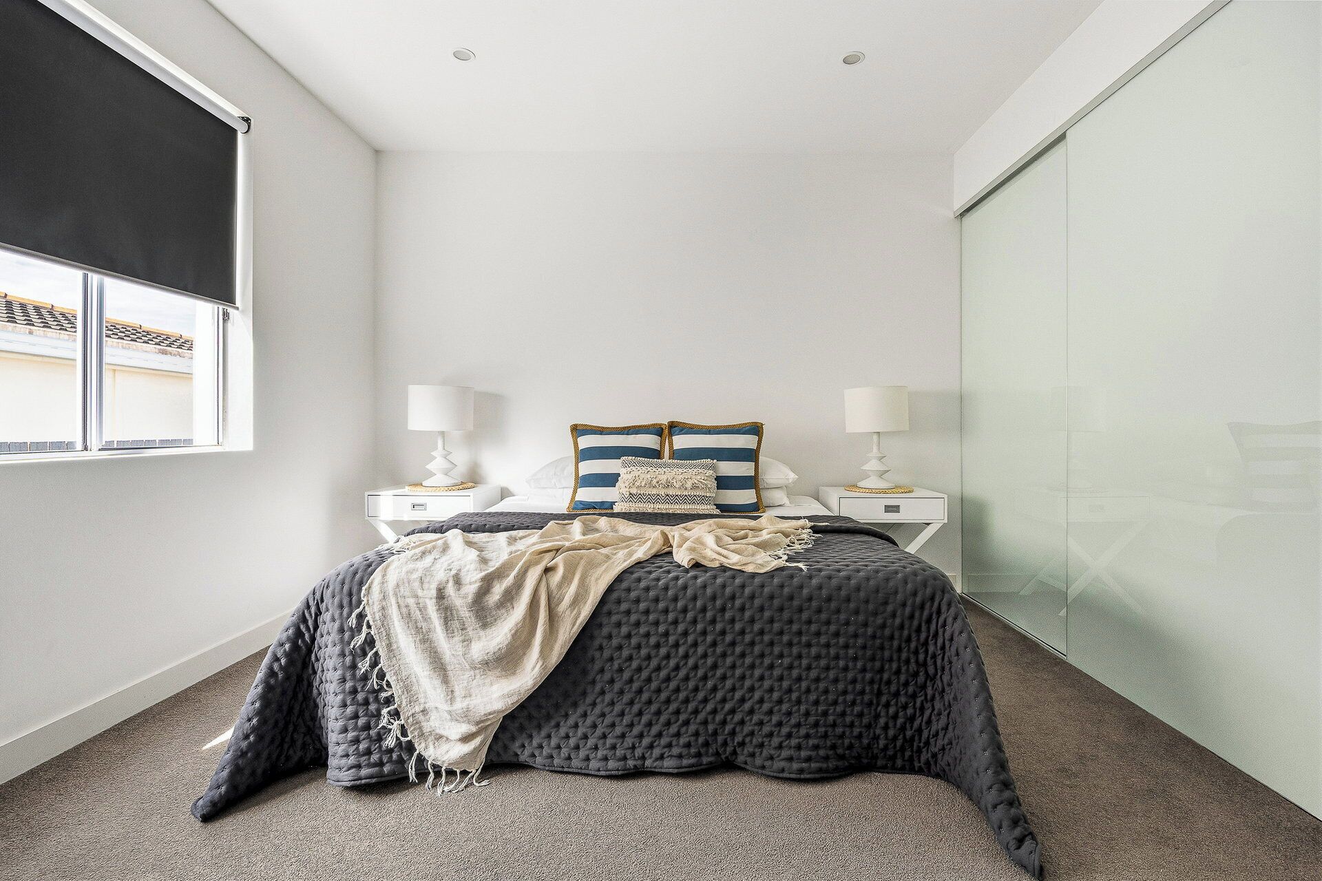 A bedroom with a bed, bedside tables, lamps, a window, and a view of the outside.