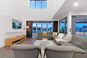 A modern living room with a sofa, coffee table, and TV, large windows with a city view, and a wooden console table.